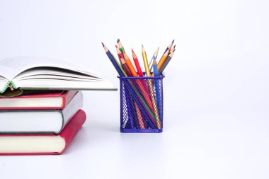 Stack of books with open book and colorful pencils on white background. Knowledge and education concept.
