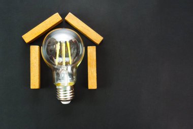 Siyah arka planda ampul olan ahşap blok şeklinde bir ev. Emlak işi, sigorta ve inşaat projesi kavramı.