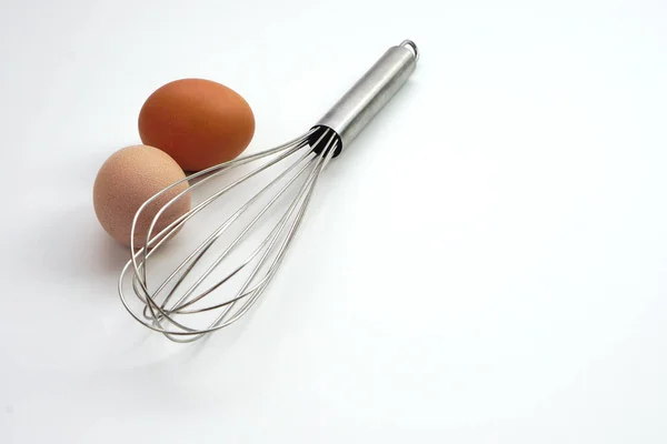 鶏の生の卵に焦点を当て 白い背景にステンレス製の卵泡立て器をぼかす パン屋用の材料又は台所用品 — ストック写真