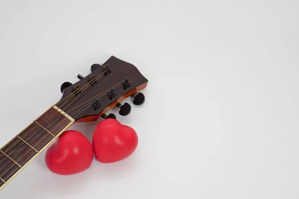 Akustik gitar ensesi ve beyaz arka plana karşı kırmızı kalp. Aşk, rahatlama ve müzik konsepti.