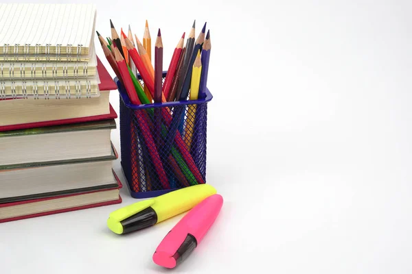 Crayon or colored pencils in box with side stack of books and school supplies on with background. Learning, study and office equipment concept.
