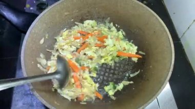 Cooker, sulu sebzelerden sağlıklı bir vejetaryen yemeği hazırlıyor ve kızartma tavasında çeşitli renkli sebzeleri karıştırıyor..