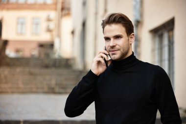 İyi giyimli bir adam tarihi bir sokakta yürüyor, telefonuyla konuşuyor ve günün tadını çıkarıyor..