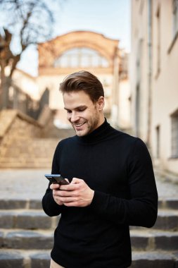 Şık bir adam akıllı telefonuyla konuşurken büyüleyici bir şehir caddesinde gülümsüyor..