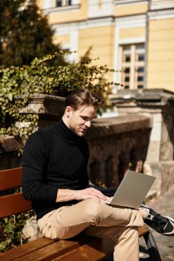 Yakışıklı bir adam bir bankta otururken dizüstü bilgisayarıyla meşgul olarak rahatça yürür..