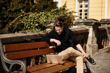 Şık bir adam güzel bir açık hava ortamında dizüstü bilgisayarına dalmış bir şekilde rahatça yürür..