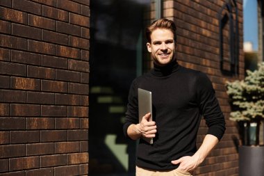 Kendine güvenen bir adam elinde dizüstü bilgisayarla gezer, şık giyinir, gününün tadını çıkarır..