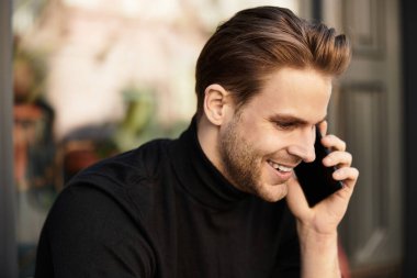 Çekici bir adam, güzel bir günde gülümseyerek ve telefonda sohbet ederek gezinir..
