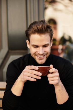 Neşeli bir gülümsemesi olan yakışıklı adam şehirde dolaşırken sıcak bir içki yudumluyor..