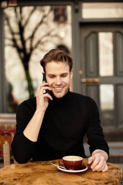 Tarz sahibi gülümseyen bir adam kahve içerken bir telefon görüşmesi yapar..