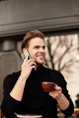 Yakışıklı bir adam telefonda konuşuyor, kalabalık bir kafede kahvesini içiyor..