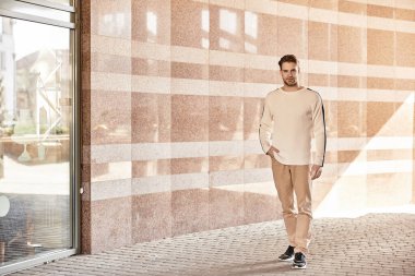 Şık bir adam, sıcak güneşin ve şehir manzarasının tadını çıkararak çağdaş bir yürüyüş yolunda yürüyor..