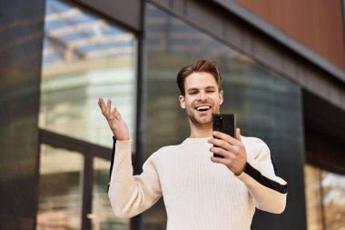 Kendine güvenen bir adam, akıllı telefonuyla neşe içinde şehir ortamında gezinir..