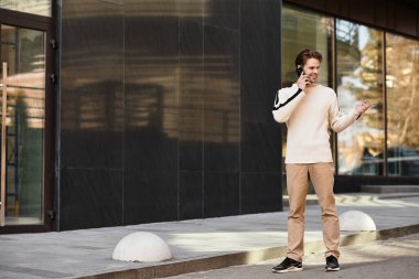 Şık bir adam kaldırımda yürüyor, modern binaların yakınında telefonla konuşuyor..