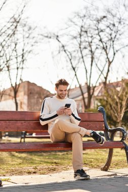 Neşeli adam hayat dolu bir parkta yürüyor, akıllı telefonuyla güzel manzaranın ortasında..