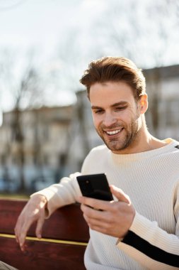 Şık bir genç adam, canlı bir şehirde telefonuna bakarken gülümsüyor..