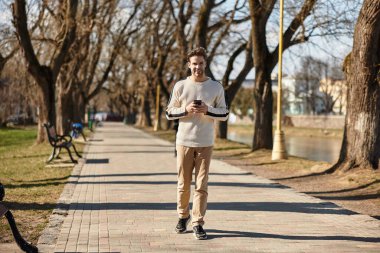 Yakışıklı bir adam ağaçlar ve güneş ışığıyla çevrili manzaralı bir yolda yürüyor..