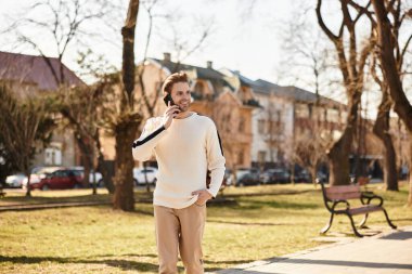 Yakışıklı bir adam neşeli bir parkta yürüyor, açık günışığı altında bir telefon görüşmesi yapıyor..