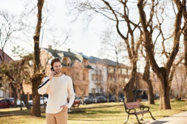 Gülümseyen adam güneşli bir parkta gezer, telefonuyla canlı bir sohbete girişir..