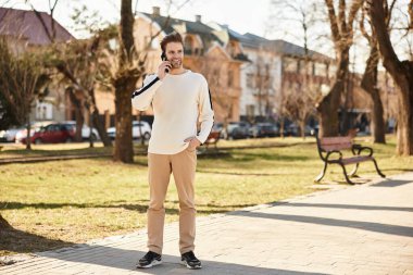 Şık bir adam parkta gezer, açık gökyüzünün altında bir telefon görüşmesi yapar..