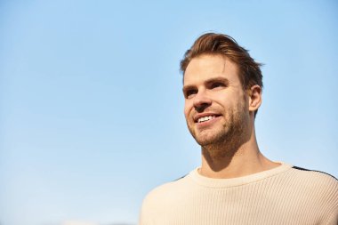 Çekici bir adam, kendine güven ve neşe saçan, masmavi gökyüzünün altında sakin bir şekilde yürümekten zevk alır..