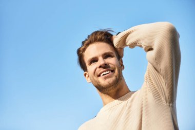 Kendine güveni tam yürüyen çekici bir adam saçlarına dokunurken gülümsüyor..