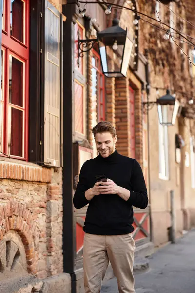 Şık bir genç adam tuhaf bir sokakta yürüyor, akıllı telefonuna odaklanmış, hafifçe gülümsüyor..
