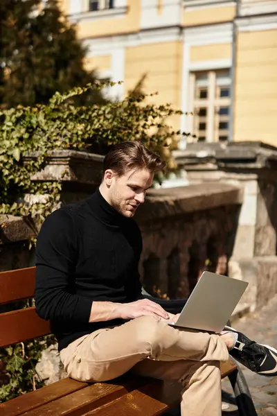 Yakışıklı bir adam bir bankta otururken dizüstü bilgisayarıyla meşgul olarak rahatça yürür..