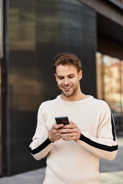 Красивый мужчина прогуливается по городу, занимается телефоном и наслаждается солнечным днем на открытом воздухе..
