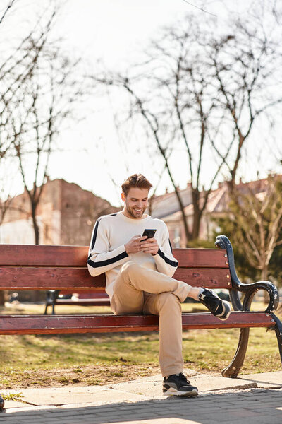 Веселый человек проходит через оживленный парк, поглощенный своим смартфоном среди красивых пейзажей.