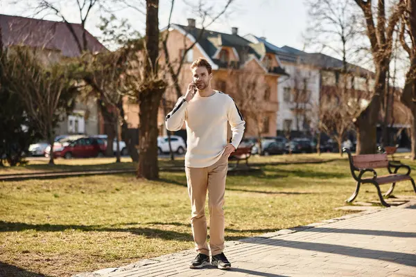 Şık bir adam güneşli bir şehir parkında telefonuyla sohbet ediyor..