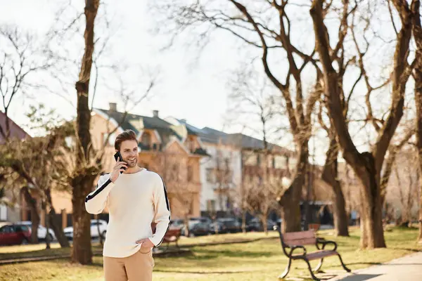 Gülümseyen adam güneşli bir parkta gezer, telefonuyla canlı bir sohbete girişir..