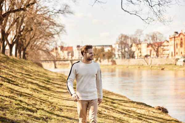 A handsome man enjoys a leisurely walk along the riverbank, soaking in the warm afternoon sun.