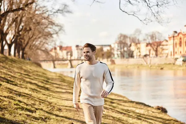 Yakışıklı bir adam nehir kenarında gezer, güneşin altında güneşlenir ve sakin bir atmosferde.
