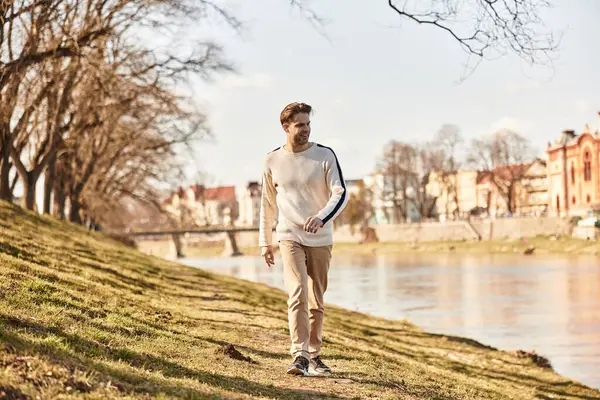 Şık bir beyefendi sakin bir nehrin kenarında rahatlık ve çekiciliğin somutlaştığı sakin bir yürüyüşün tadını çıkarır..