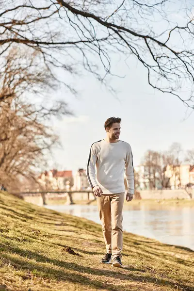 Çekici bir adam nehir kıyısında geziniyor, ılık güneşin ve huzurun tadını çıkarıyor..