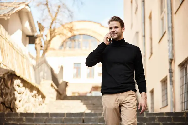 A handsome man walks confidently down the steps, chatting on his phone in bright daylight. — Stock Photo