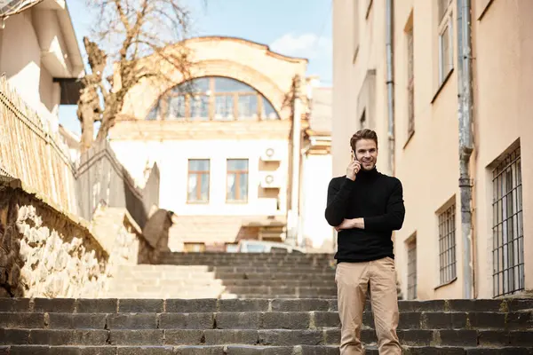 A well dressed man walks down stone steps, engaged in a phone conversation under clear skies. — Stock Photo