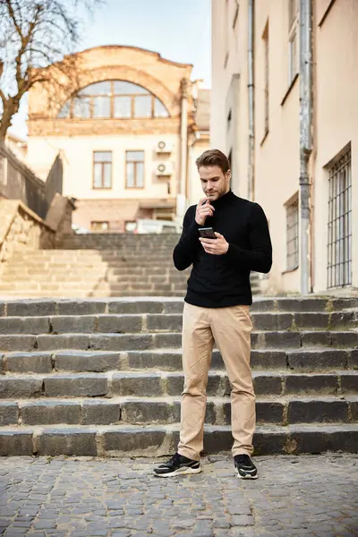 Un hombre guapo camina por escalones de piedra, absorto en su teléfono, disfrutando de un día soleado. - foto de stock