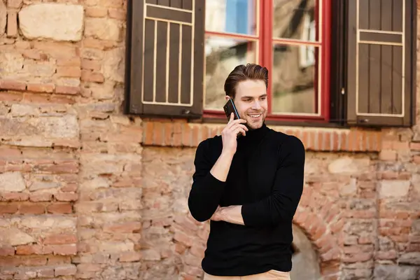 A stylish man strolls along a charming street, engaged in a lively phone conversation. — Stock Photo