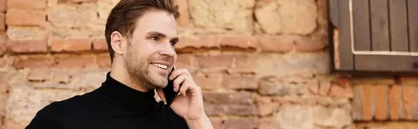 Un uomo elegante cammina tranquillamente, parlando al telefono su uno sfondo di mattoni rustici. — Foto stock