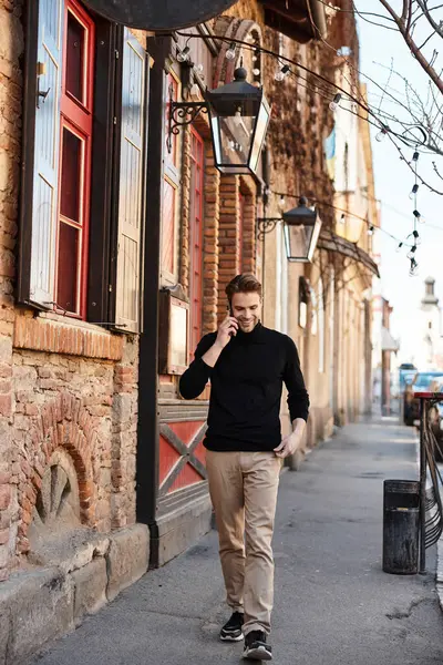 A stylish man walks down a picturesque street, chatting on the phone amid unique architecture. — Stock Photo
