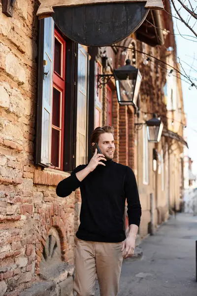A well dressed man walks casually along a charming street, engaged in a phone call while smiling. — Stock Photo