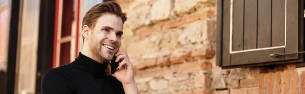 Un uomo elegante cammina casualmente, chiacchierando al telefono su uno sfondo rustico muro di mattoni. — Foto stock
