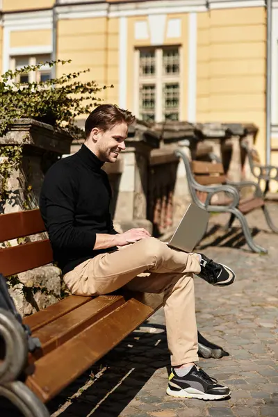 A handsome man takes a break from walking to engage with his laptop on a sunny day near benches. — Stock Photo