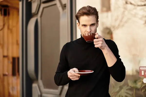 A confident man sips from a cup, taking a moment during his stroll in the lively street. — Stock Photo