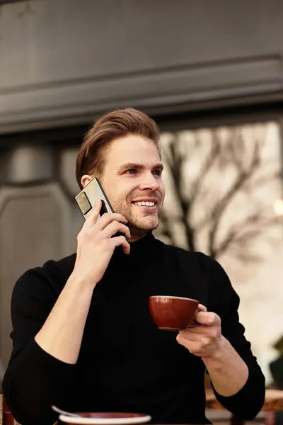 A handsome man talks on the phone, enjoying his coffee in a busy urban cafe. — Stock Photo