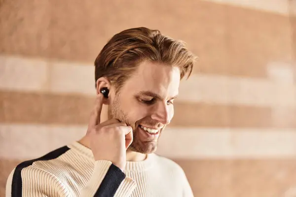 Un bell'uomo passeggia in una zona moderna, sorridendo e ascoltando musica con auricolari. — Foto stock