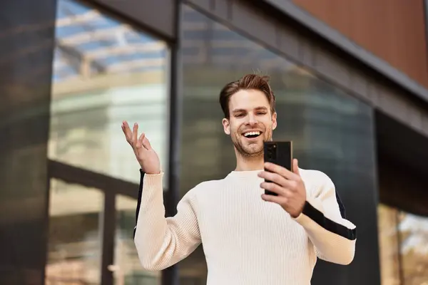 Ein selbstbewusster Mann schlendert durch eine urbane Umgebung und interagiert freudig mit seinem Smartphone. — Stockfoto