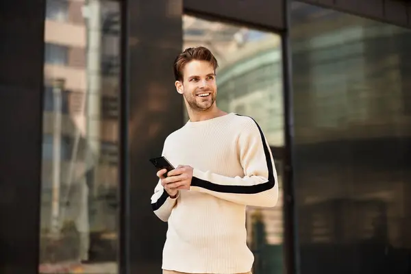 Ein stilvoller Mann schlendert durch eine städtische Umgebung, checkt sein Handy und lächelt fröhlich. — Stockfoto